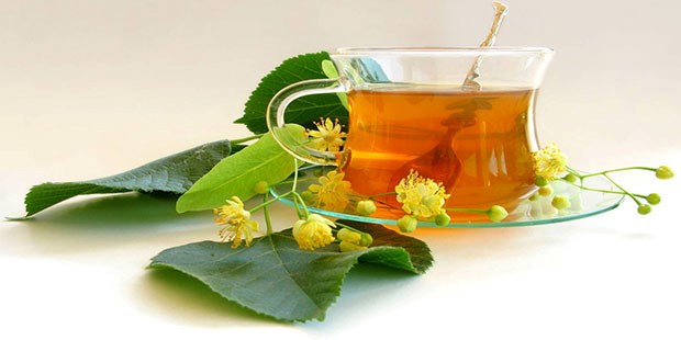 Липовый мед в прозрачной стеклянной чашке с ложкой, вокруг листья и цветы липы.