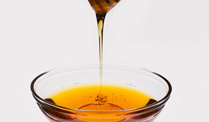 Гречаний мед стікає з ложки в скляну тарілку, яскраво переливається темними тонами на світлі
